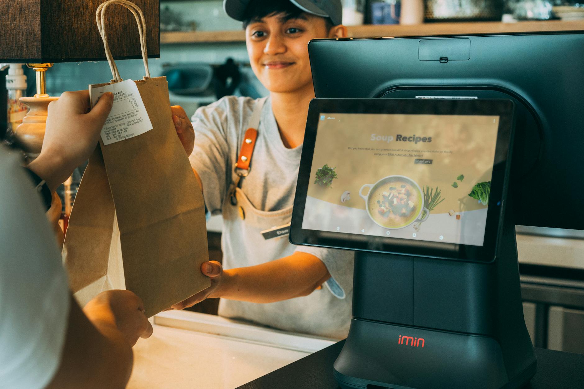 Photo by iMin Technology on <a href="https://www.pexels.com/photo/smiling-employee-giving-a-paper-bag-with-receipt-to-a-customer-12935094/" rel="nofollow">Pexels.com</a>